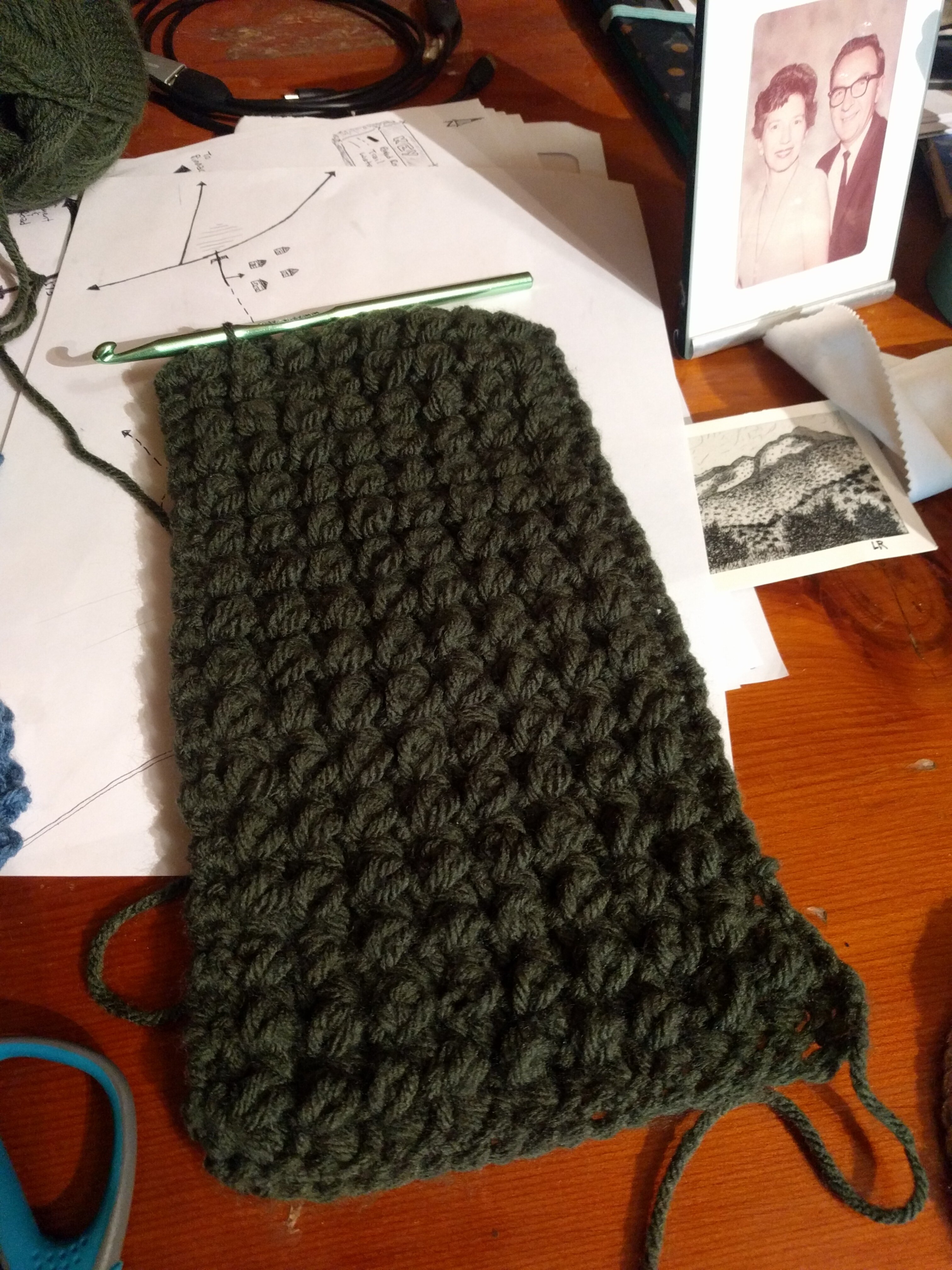 An unfinished dark-green crocheted scarf