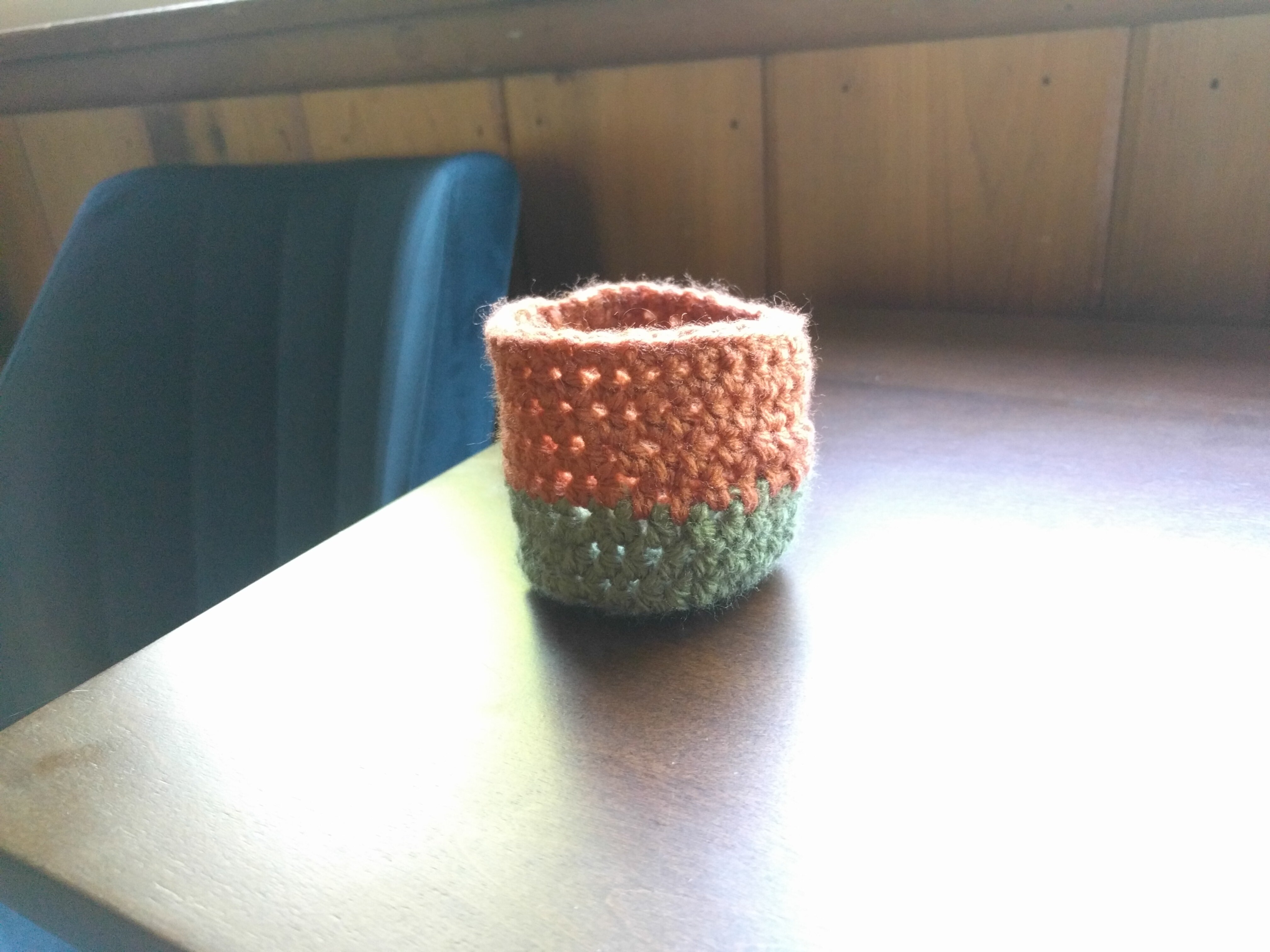 A small crochet sage-green and red-brown basket a few inches in diameter