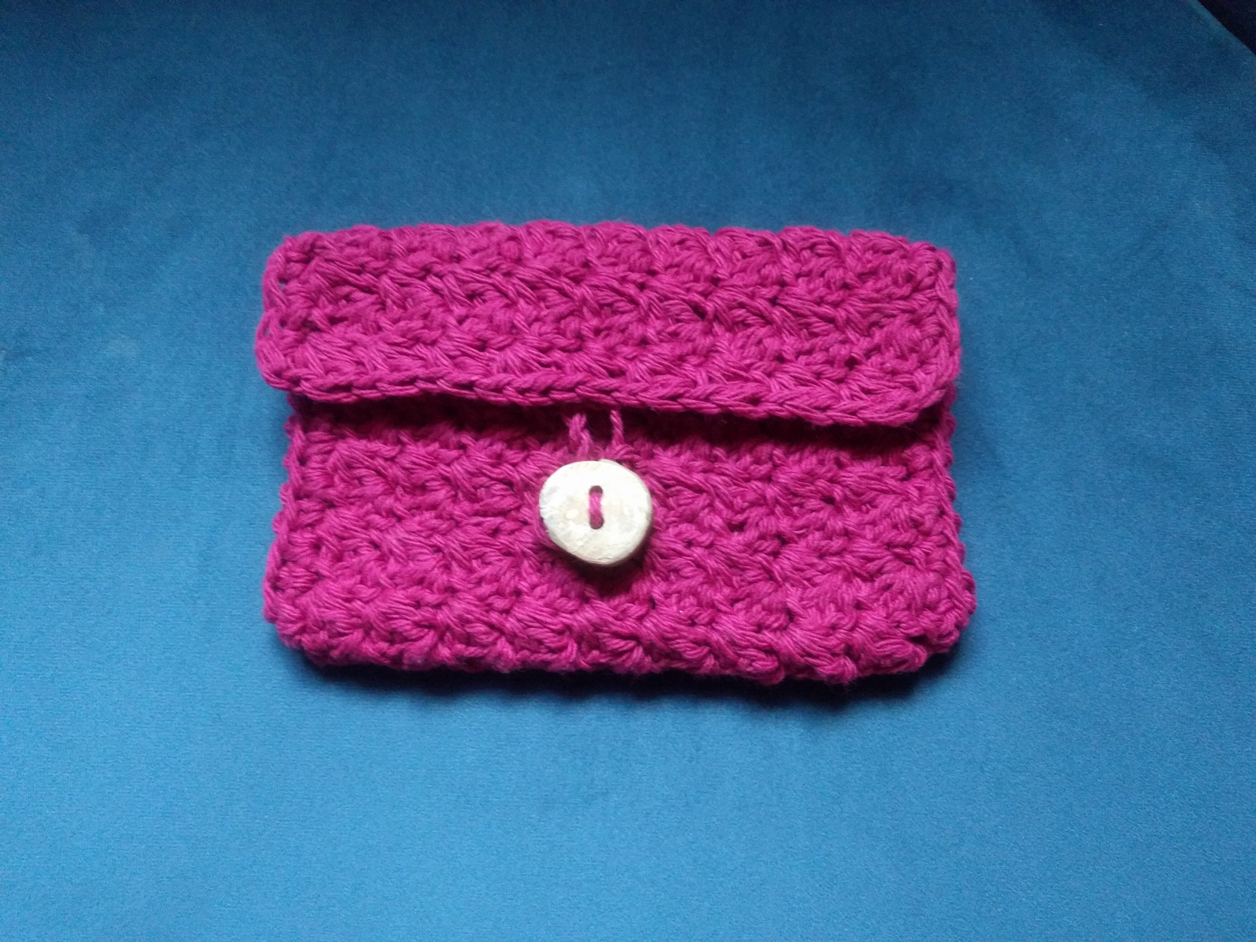 A redish-purple crocheted wallet with its flap closed and buttoned