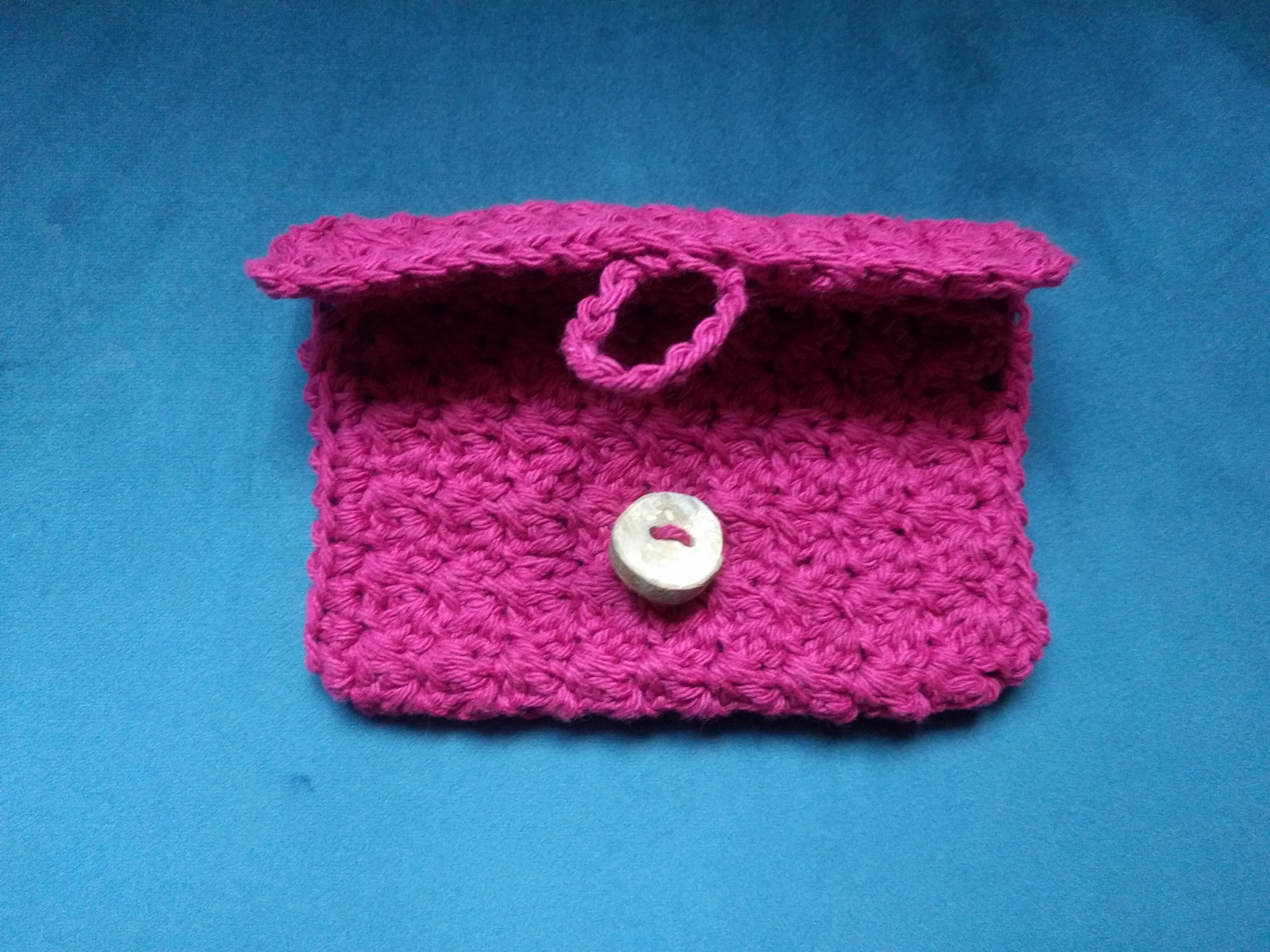 A redish-purple crocheted wallet with its flap unbuttoned